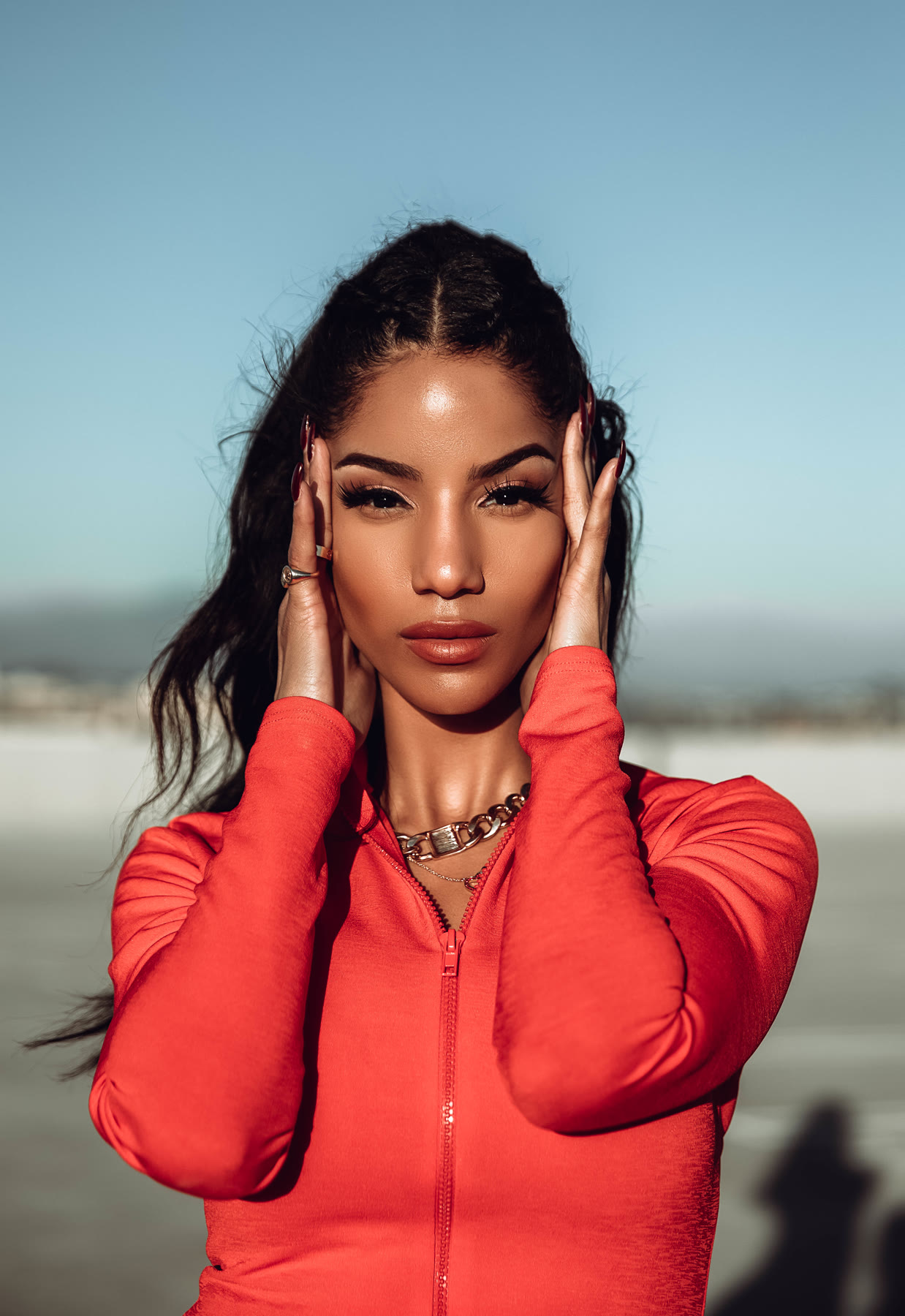 Close portrait of Christal in a red zip top, hands framing her face