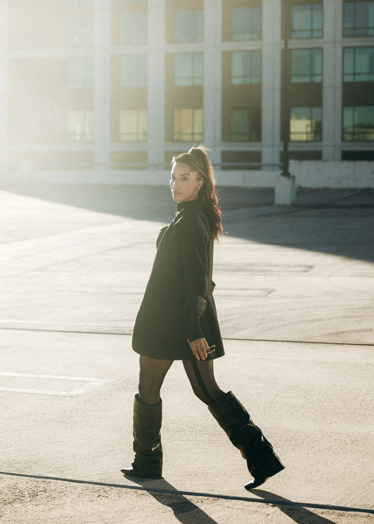 Christal walking across a sunlit rooftop in a black blazer dress and slouch boots