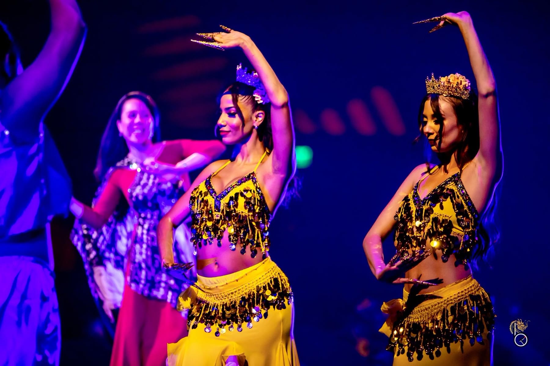 Christal performing on stage in a gold coin costume and crown under purple stage lights