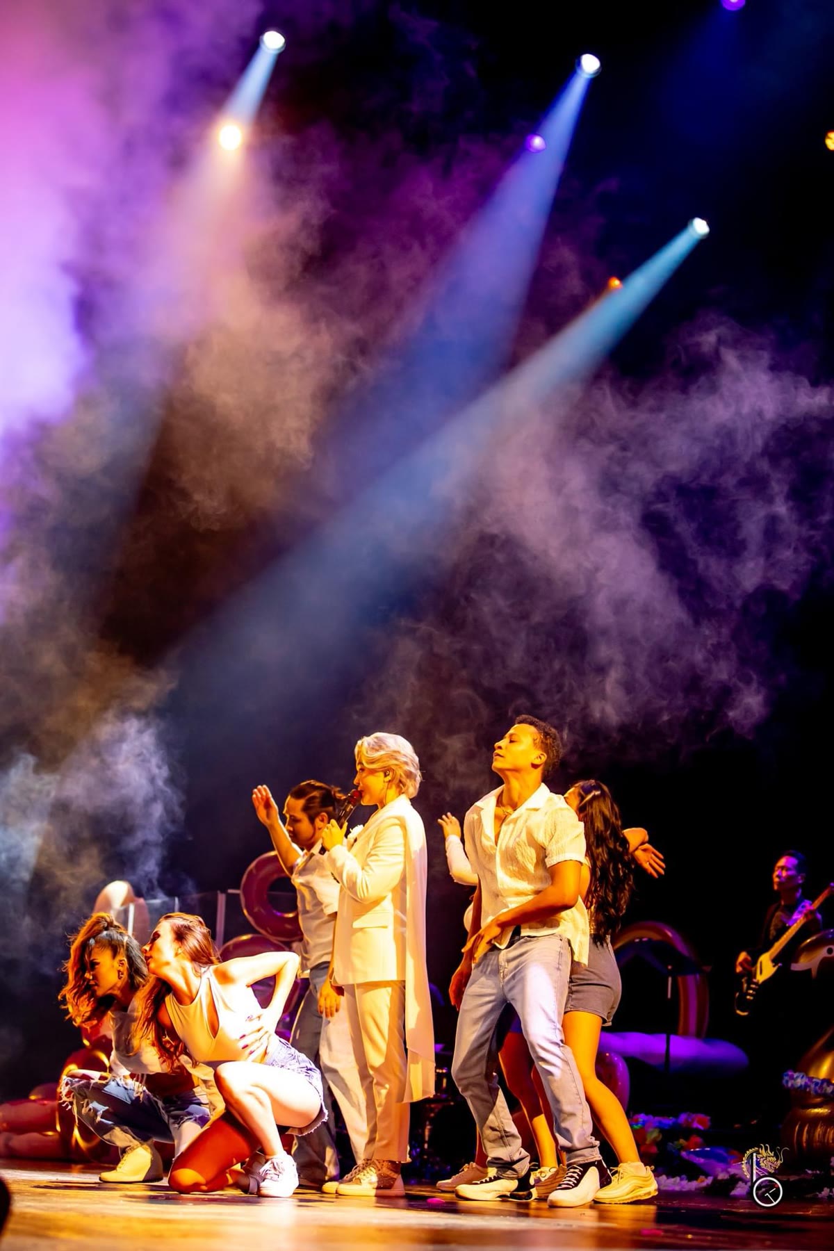 Christal performing on stage with a dance ensemble in white and denim under haze and spotlights