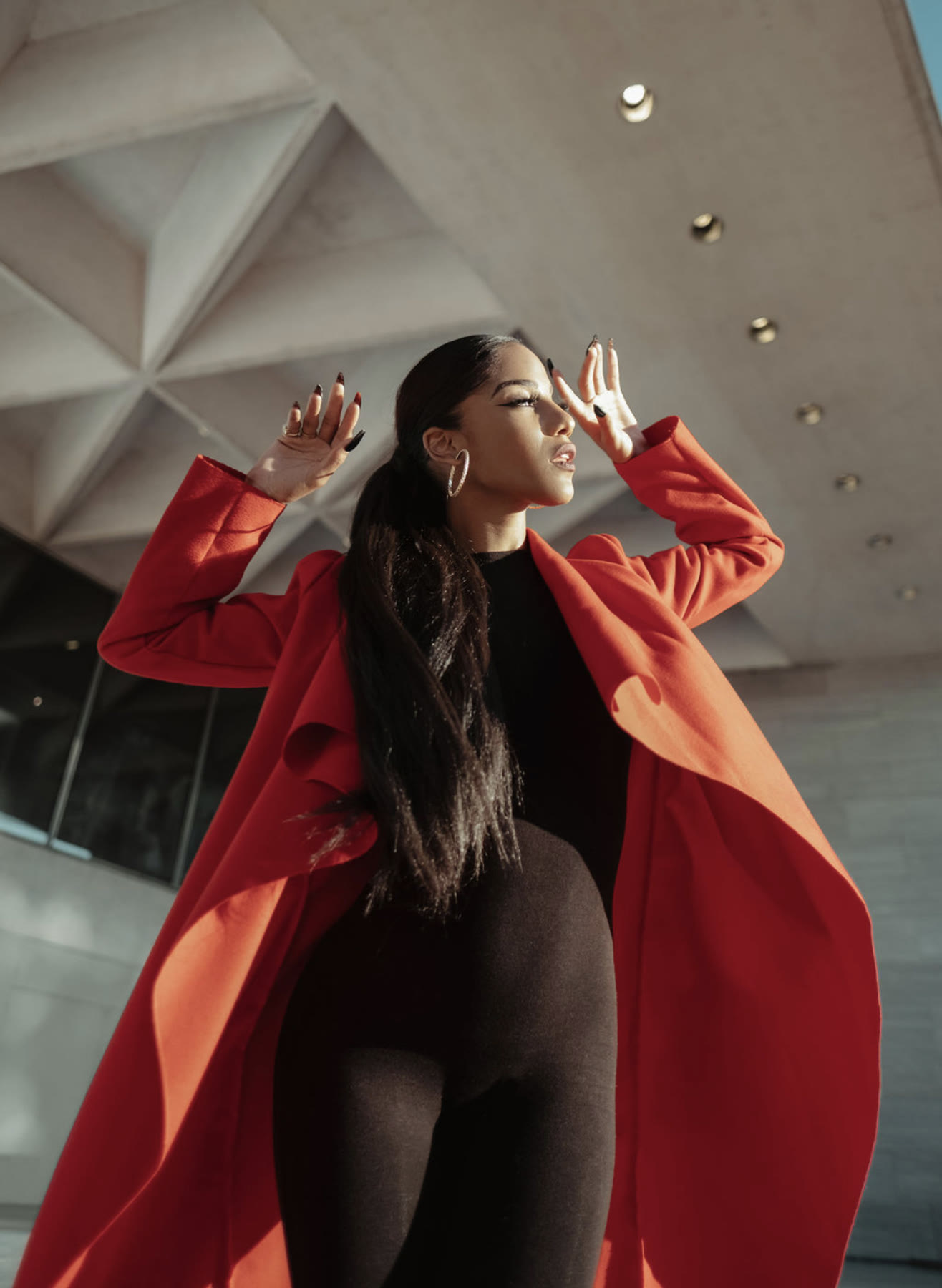 Low-angle shot of Christal in a red coat, hands framing her face