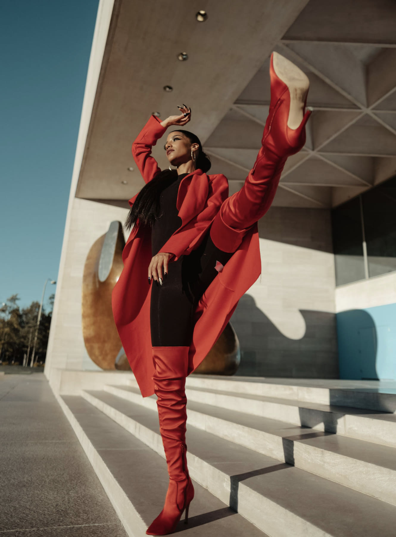 Christal in a high kick wearing a red coat, black bodysuit and red thigh-high boots on museum steps