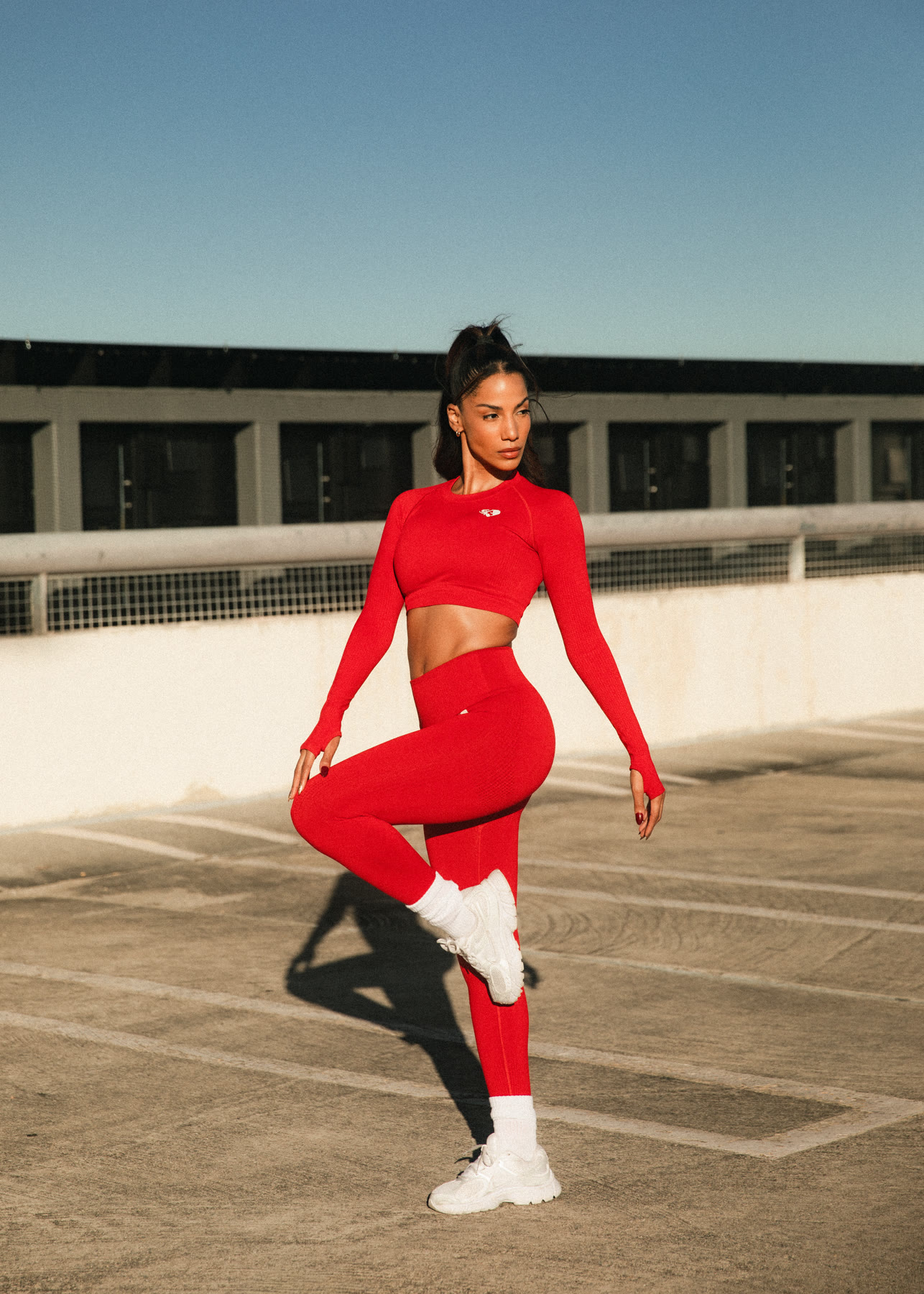 Christal balancing on one leg, knee raised, in a red activewear set