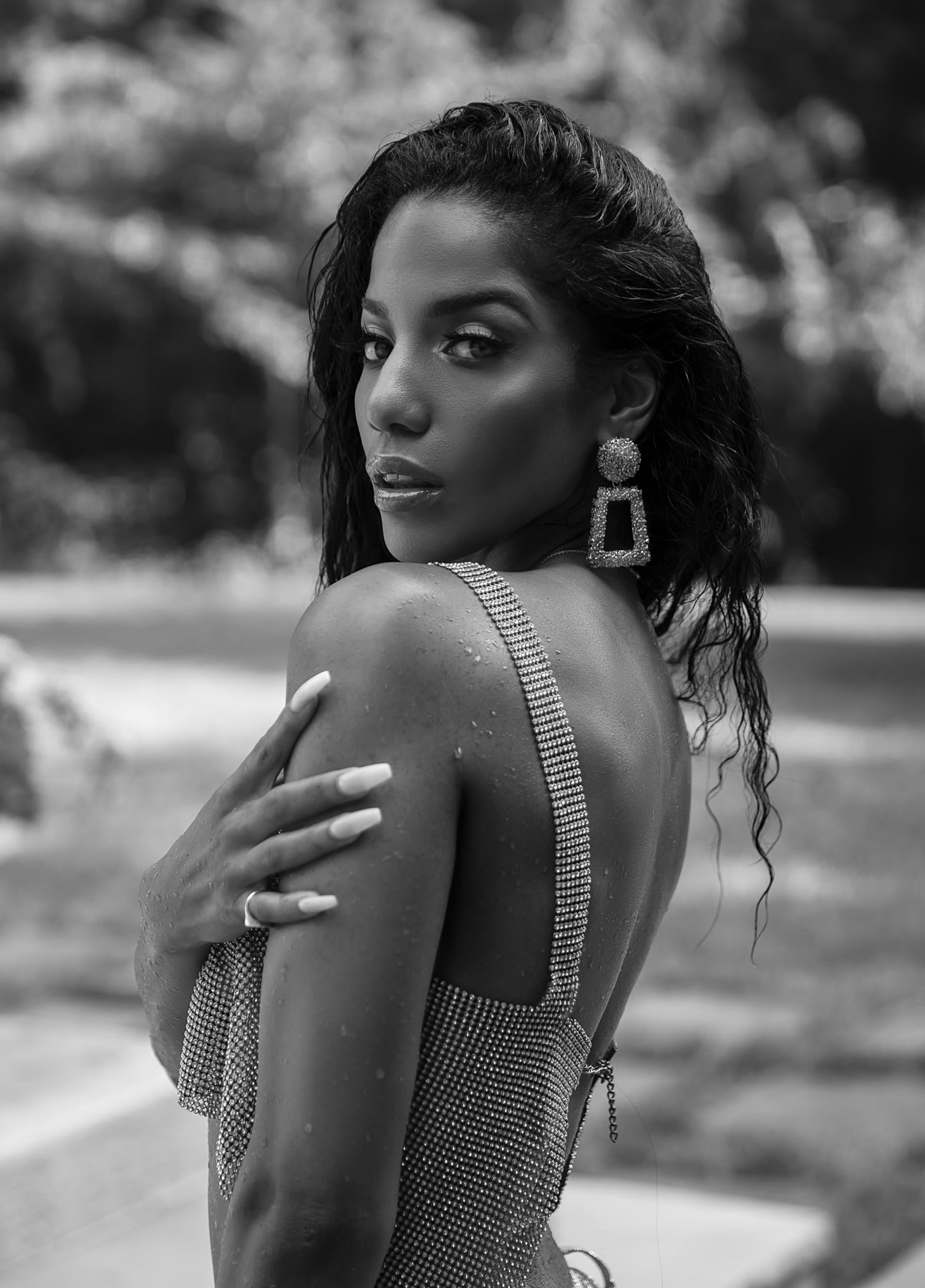 Black-and-white portrait of Christal glancing over her shoulder in a crystal mesh top, wet hair and statement earrings