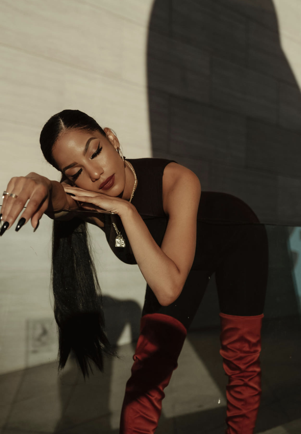 Christal leaning forward, head resting on her hands, eyes closed, black bodysuit and red boots