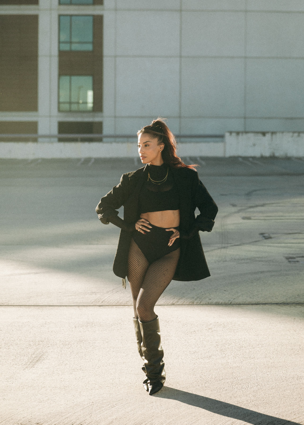 Christal standing on a rooftop in an oversized black blazer, fishnets and slouch boots