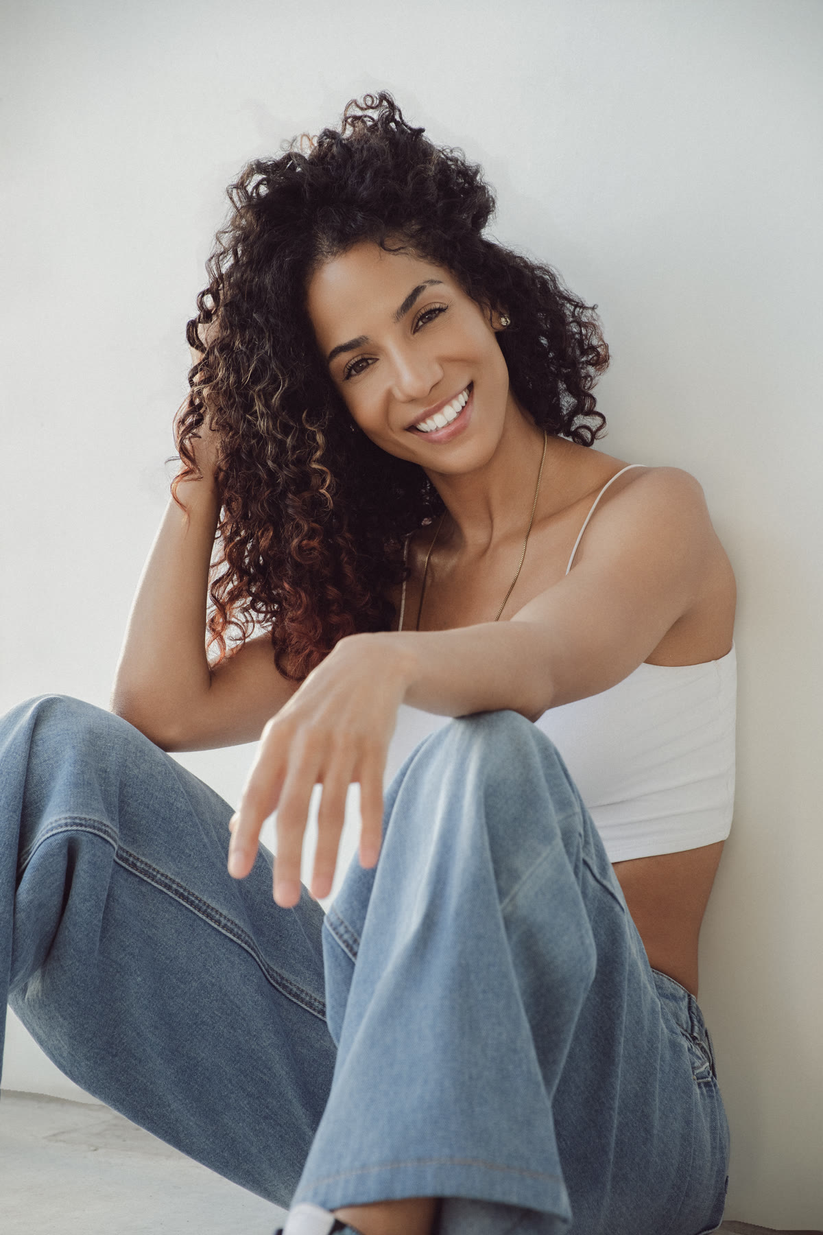 Christal sitting on the floor against a white wall, smiling and reaching toward the camera