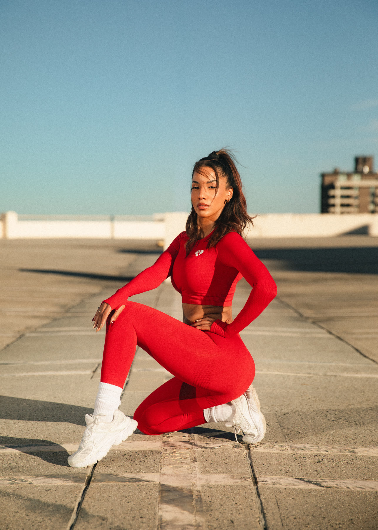 Christal kneeling on a rooftop in a red activewear set