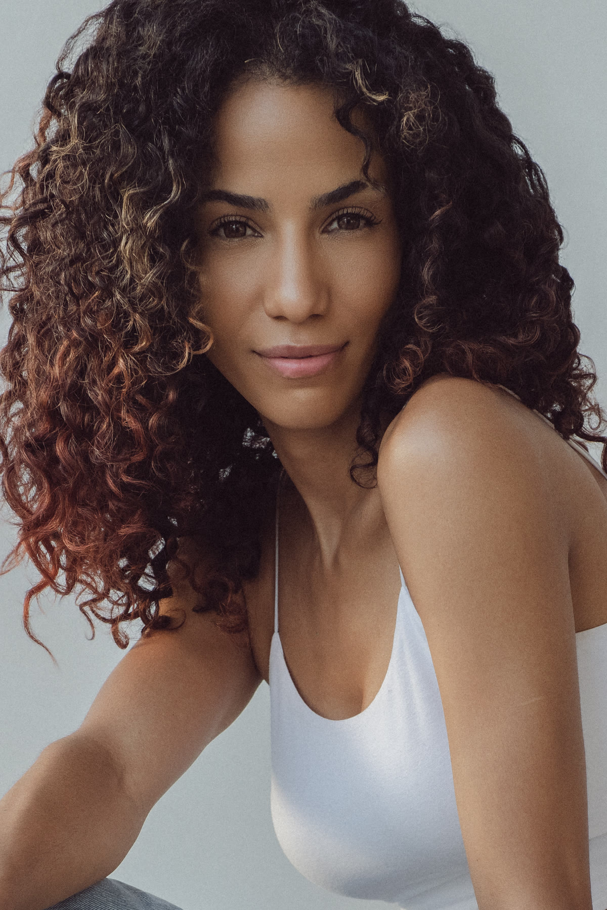 Close headshot of Christal with curly hair, soft smile, white camisole