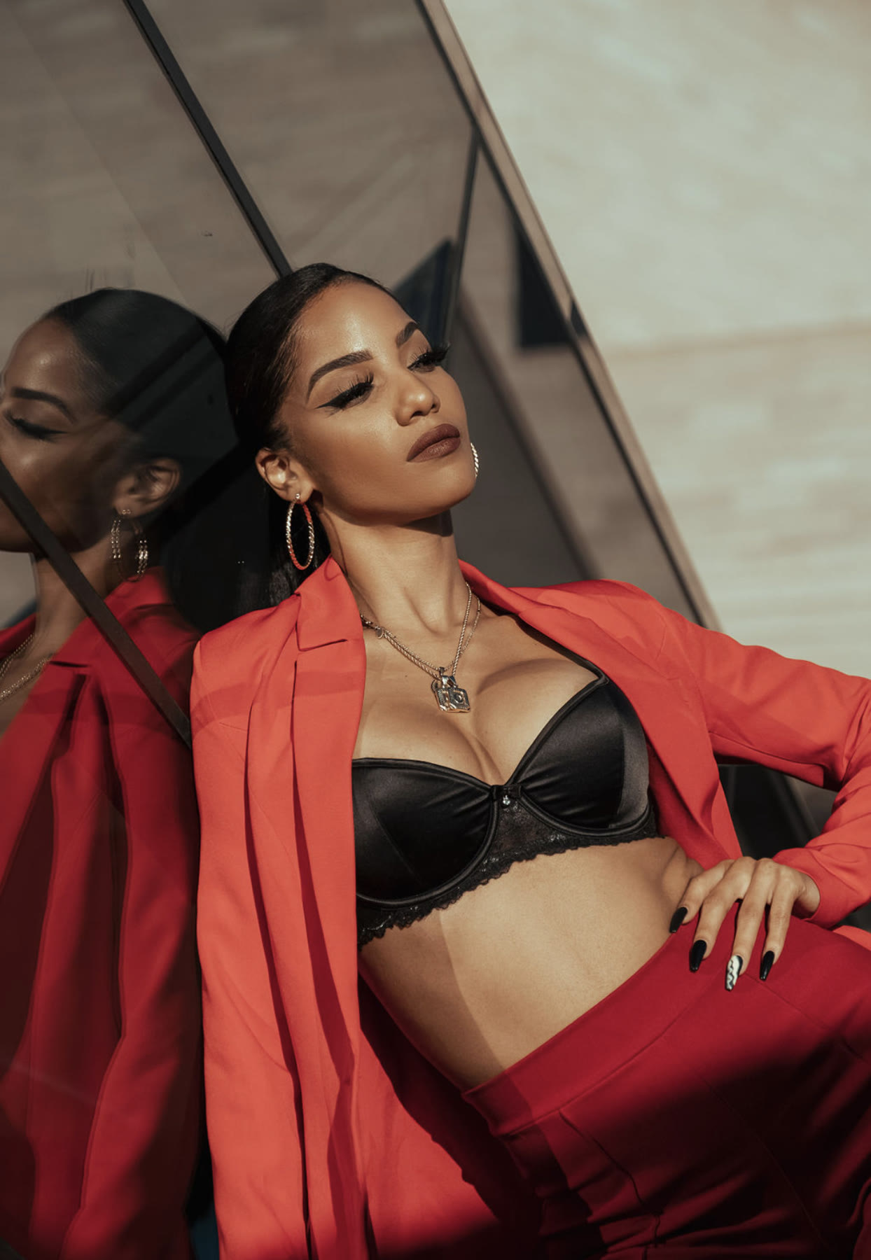 Christal in a red blazer leaning against a mirrored wall, reflection beside her