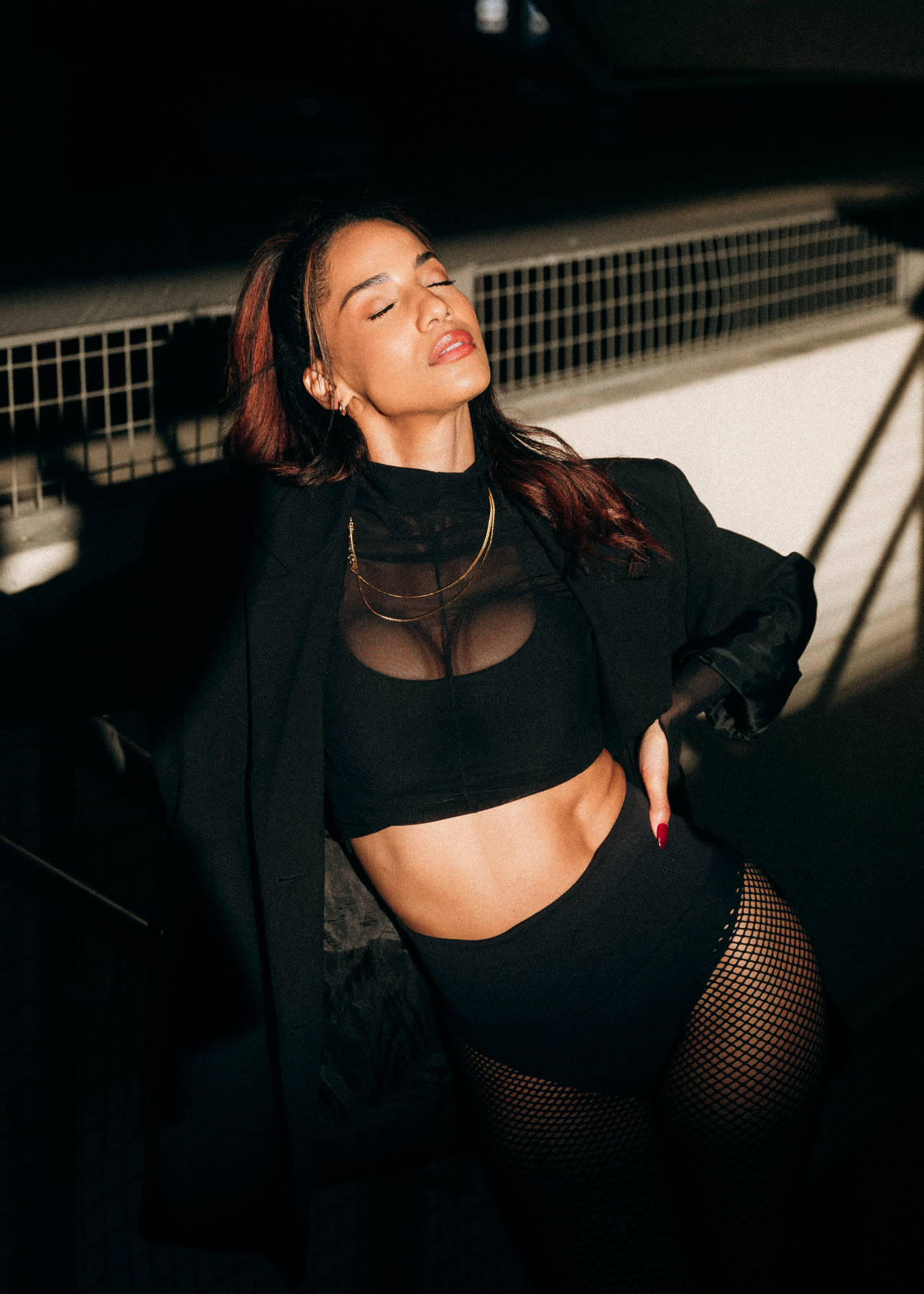 Christal with eyes closed in a black mesh crop top and blazer, golden light