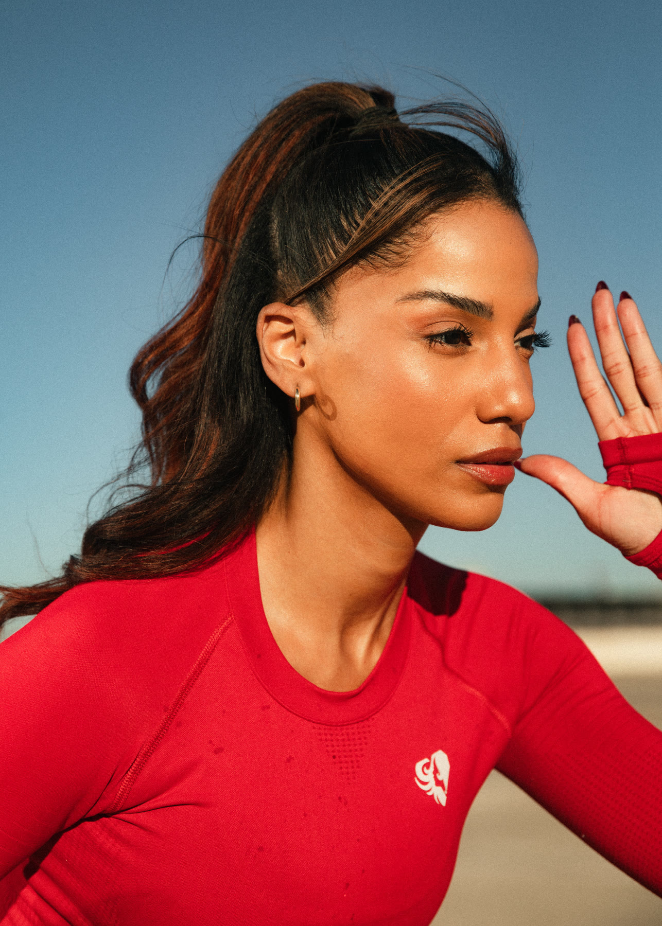 Profile close-up of Christal in a red top, high ponytail, hand raised