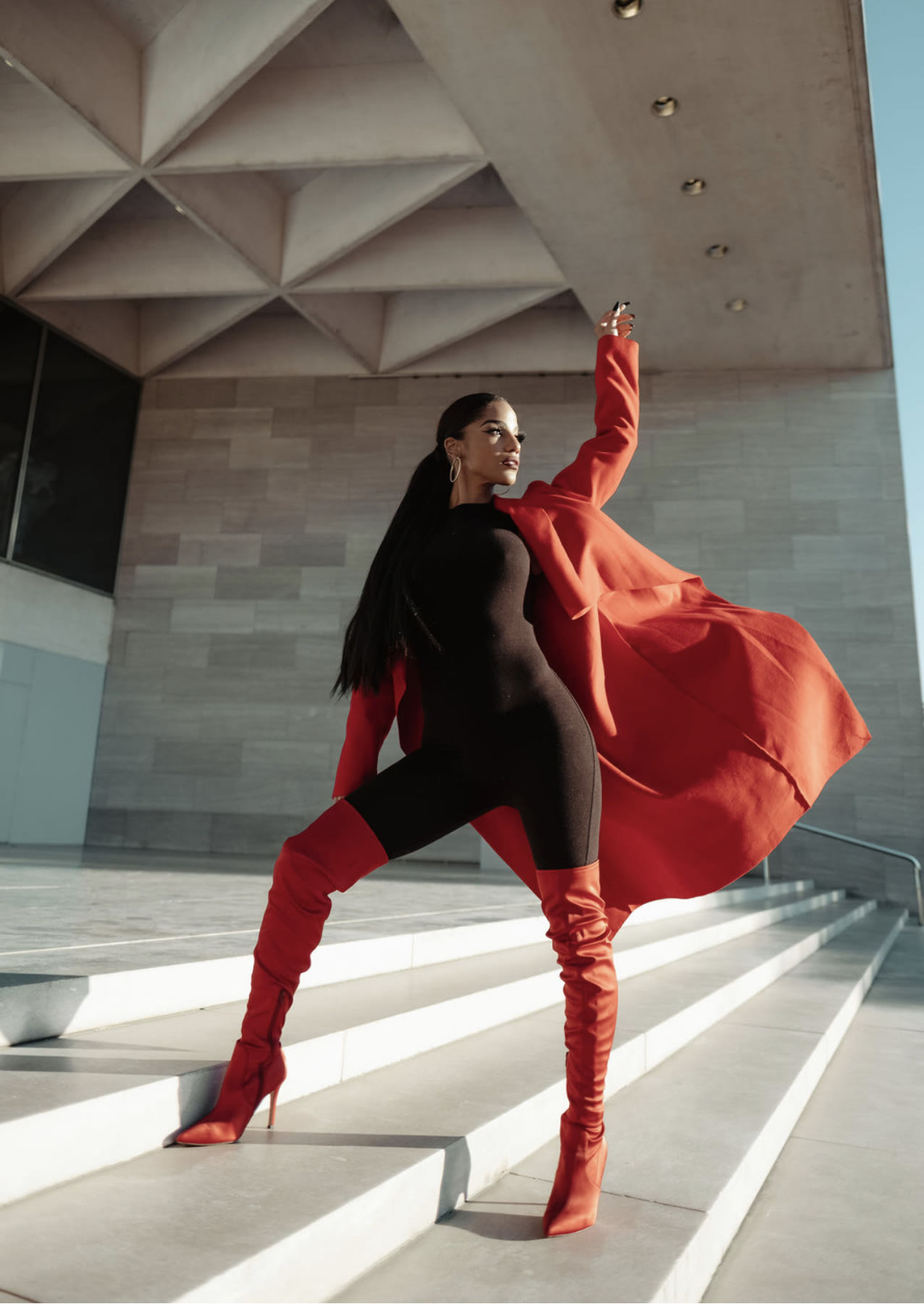 Christal posing on stone steps, red coat flowing, one arm raised